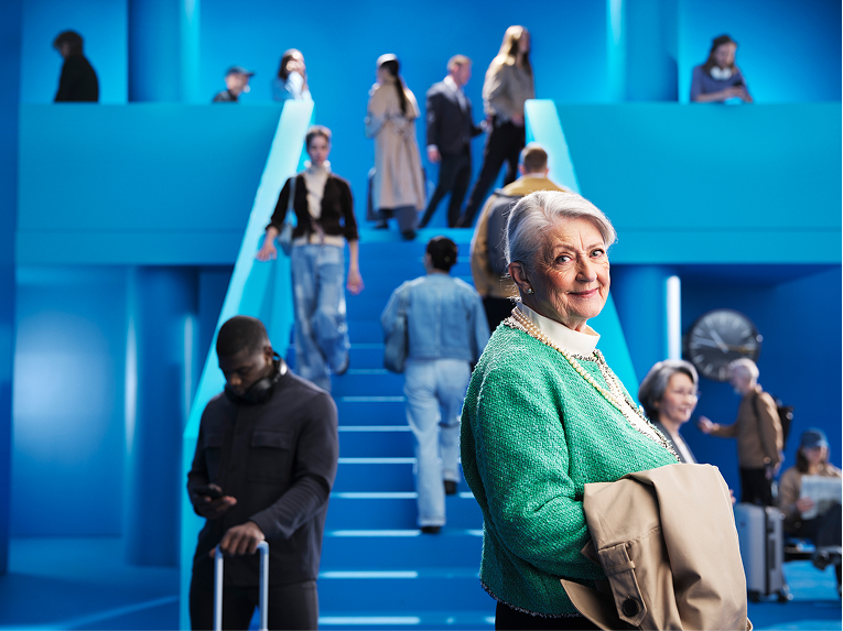 An elderly woman wearing Beltone Boost Max S hearing aids at a busy station. She is looking comfortably into the camera thanks to the Clear Focus feature.