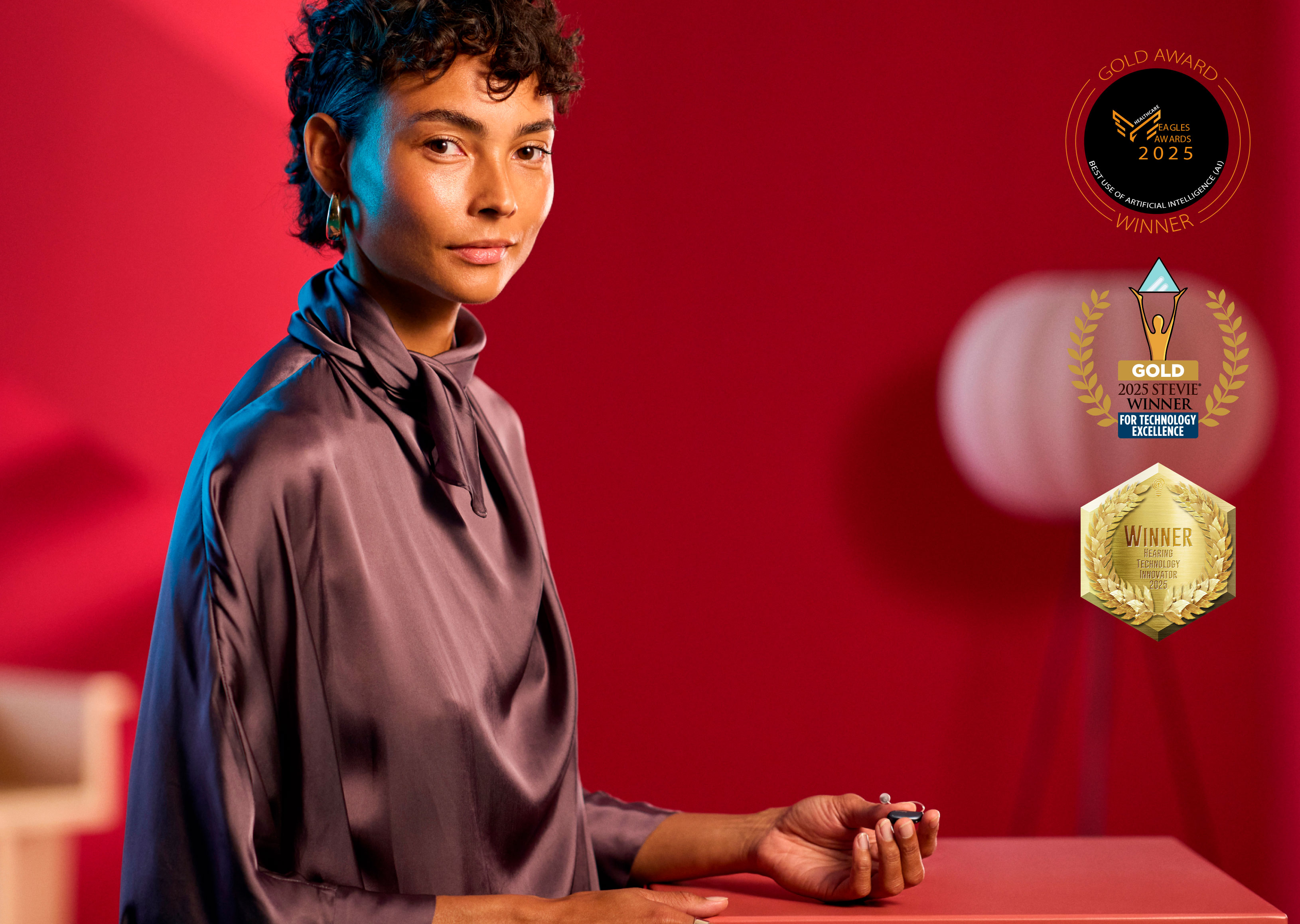 Lady sitting with a hearing aid in her hand - award badge