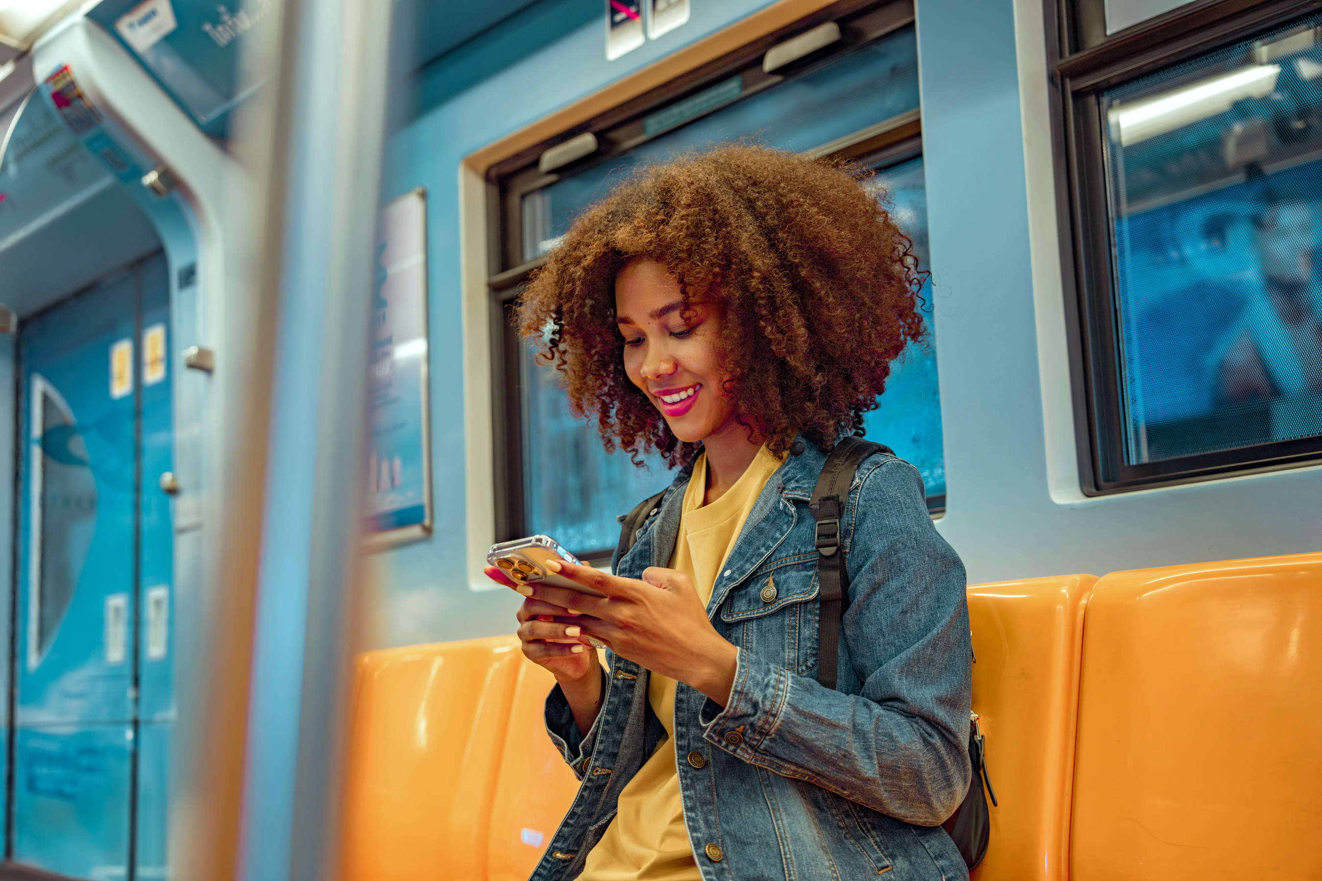 A smiling woman sits on the metro, effortlessly streaming audio directly to her Danavox Astro SP hearing aids.